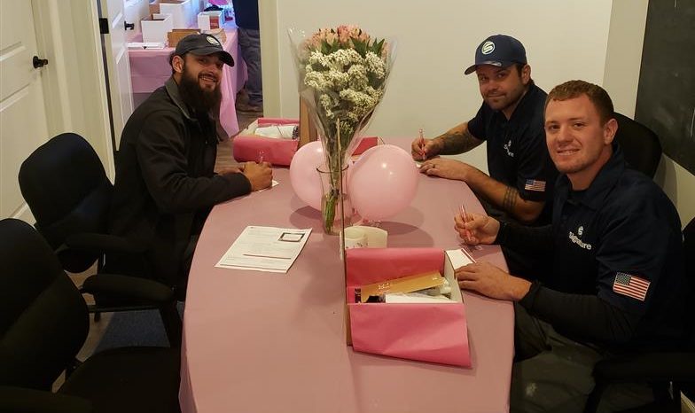 Three male employees from Signature HVAC smiling toward the camera as their write notes to Hope Kit recipients.