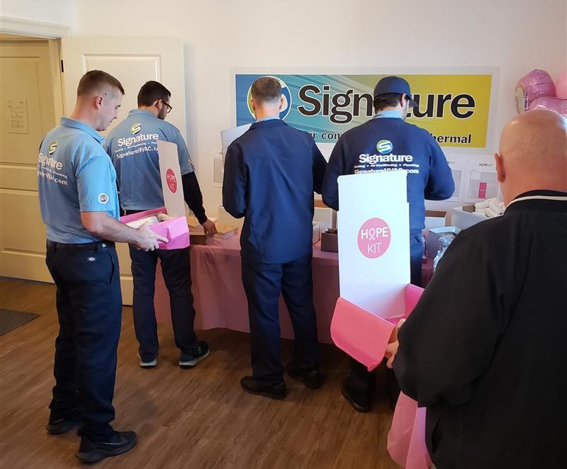 Several members of Signature HVAC crowding a table as they begin packing Hope Kits.