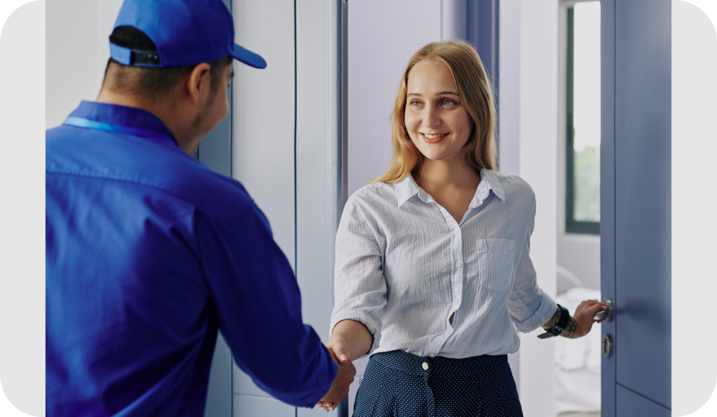 HVAC technician greeting a homeowner at the front door, shaking her hand as she welcomes him inside.