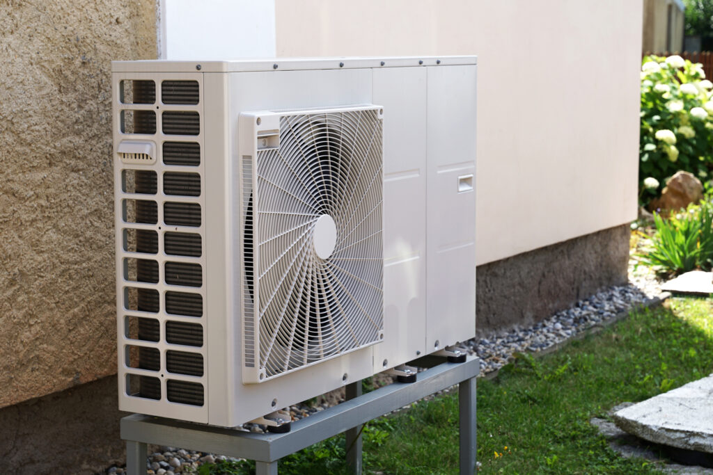 Angled view of a heat pump unit outside of a white stucco home.