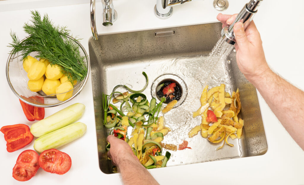 Close view of person's hands washing vegetables in a stainless steel kitchen sink.