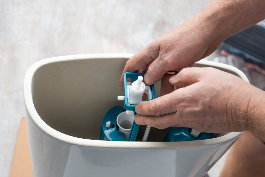 A plumber installs a water pump in a ceramic toilet cistern.