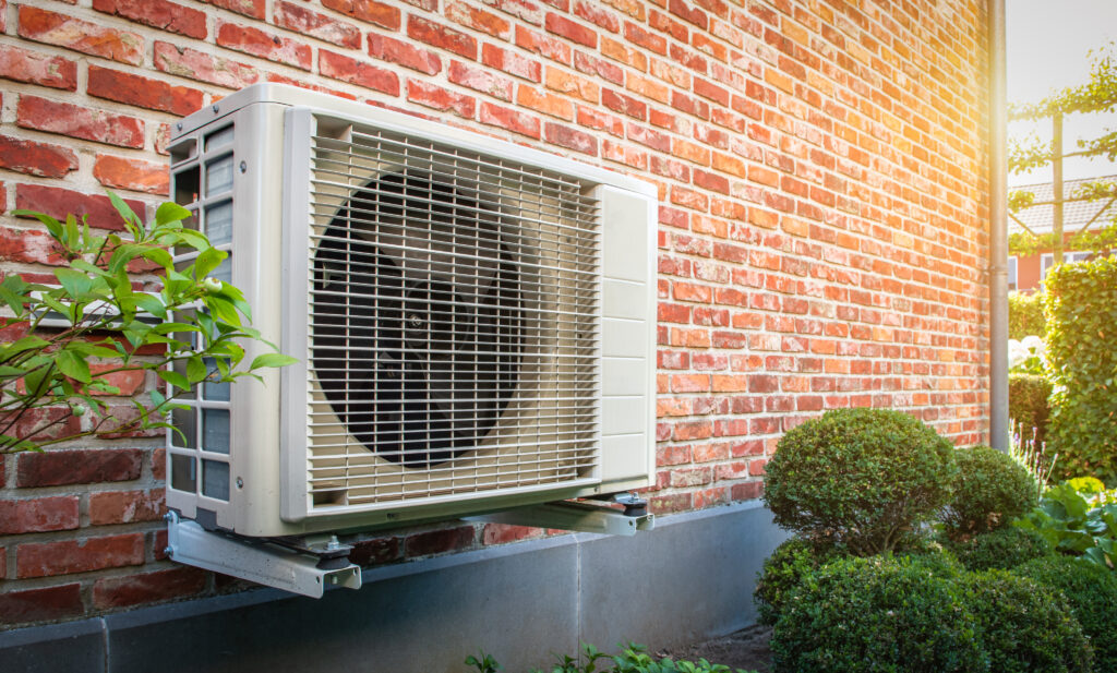 Angled view of a wall-mounted exterior heat pump unit next to a brick home.